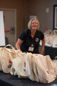 Woman smiling near table with tote bags.