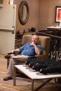 Man sitting in chair near stacked hats.