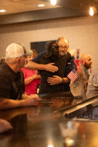 People hugging warmly at a bar counter.