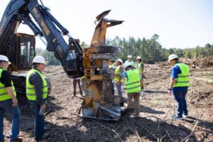 Workers inspecting machinery in a forest area.