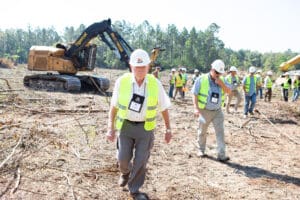 Construction crew inspects cleared land with excavator