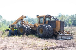 Workers inspecting large forestry vehicle on site.