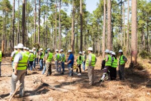 Group wearing safety vests in forest clearing.