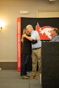 Two people hugging on stage at event.