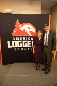 Two people standing by American Loggers sign.