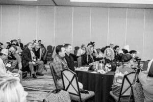 People seated at conference, wearing feathered hats.