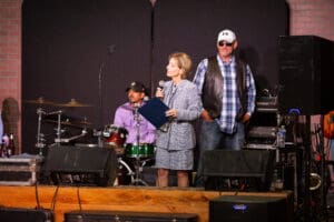 Woman speaking on stage with musicians behind.