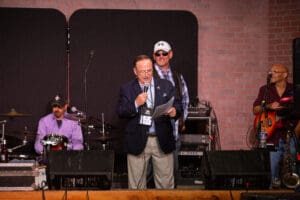 Man speaking on stage with musicians behind.