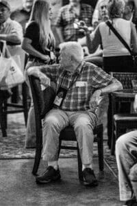 Elderly man sitting at crowded event.