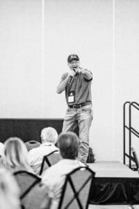 Man speaking on stage to seated audience.