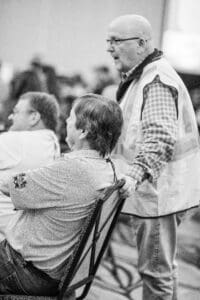 Man in vest talking to seated person.