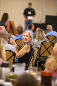 Smiling woman clapping in crowded conference room.