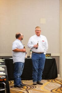 Two men talking, holding bottles indoors.