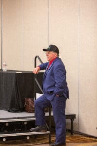 Man in blue suit leaning on stage.