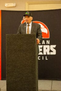 Man speaking at podium with logo background.