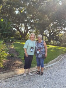 Two women posing outdoors near large trees.
