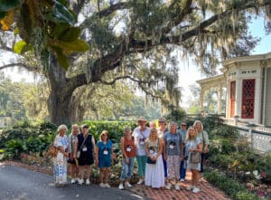 Group posing under large tree near house.