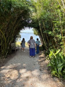 People walking through bamboo tunnel toward water.